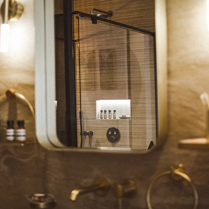 La douche à l’italienne se reflète dans le miroir, entre pierre naturelle et laiton.