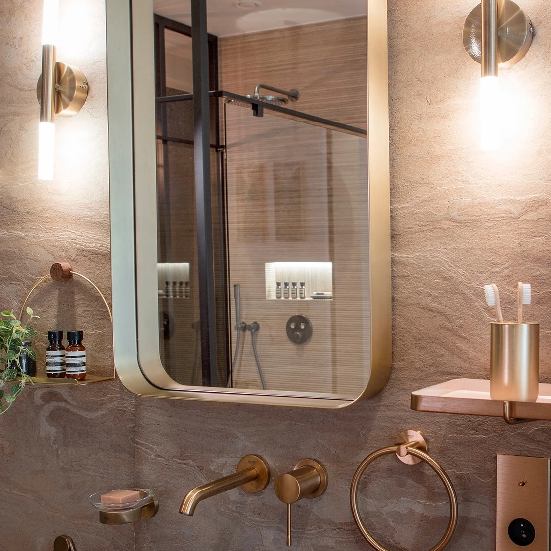 Miroir doré et vasque en pierre, avec la douche visible dans le reflet
