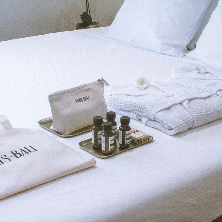 Peignoirs, trousse Paris Bali et produits d’accueil disposés sur le lit.
